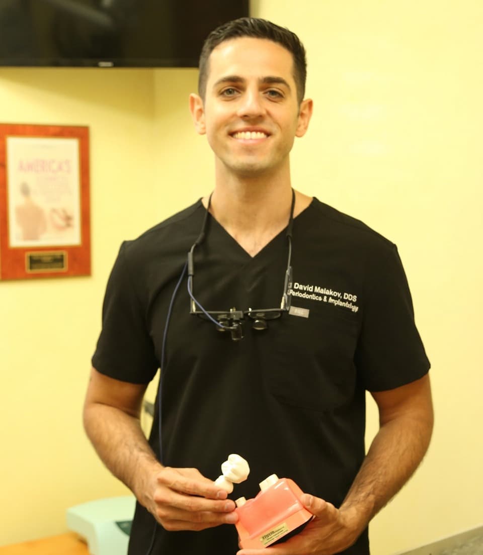 Dr. David Malakov holding a dental implant model in his Queens office
